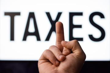 Angry man showing middle finger to screen with inscription TAXES having no desire to pay taxes