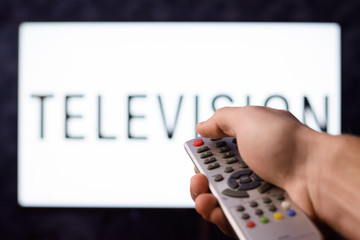 Middle aged male switches off a TV set by pushing red power button on a remote controller