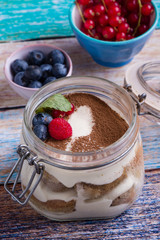 tasty tiramisu dessert in glass jar on color table