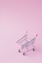 Small supermarket grocery push cart for shopping toy with wheels and pink plastic elements on pink pastel color paper flat lay background. Concept of shopping. Copy space for advertisement