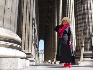 Femme avec un mateau noir et une écharpe rouge posant devant les colonnes de l'église de la Madeleine à Paris