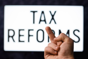 Man showing middle finger to a screen with inscription TAX REFORMS without desire to pay more taxes