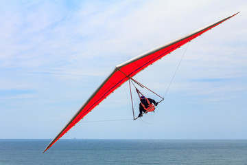 Hang gliding man flying on an orange wing at Fort Funston in San Francisco, one of the premier...