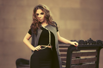 Young fashion woman in long sleeveless coat walking on city street