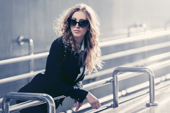 Young fashion blonde business woman in sunglasses leaning on railing