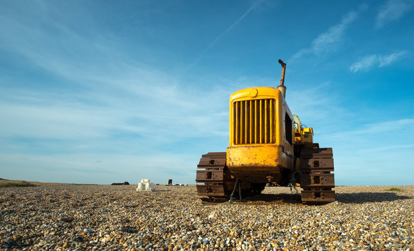 Old rusty yellow tractor unit on a pebble beach