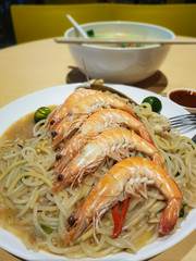 Plate of Asian street foodserved at hawker center. Udon noodles with king prawns