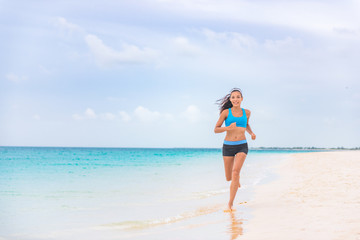 Fototapeta na wymiar Exercise fitness athlete woman jogging on beach training cardio in summer vacation background. Blue ocean water, sun sky landscape. Happy Asian girl running barefoot outside.