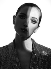Black and white portrait of trendy girl with hair pulled back and stylish makeup in a shining dress with a shadow falling on half of the face