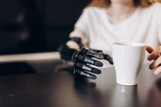 disabled girl controlling her actitions, close up cropped photo. artificial fingers touching the cup on the table, sensorics concept