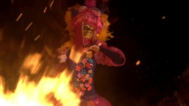a bright girl in a pink and purple dress, holds her hands to her face and spreads them to the sides, on a dark background, the operator shoots video through the flame.