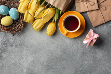 Yellow tulips in a paper bag, a nest with Easter eggs on a wooden background. Top view with copy space.