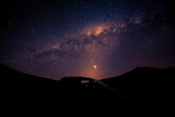 Fototapeta na wymiar Silhouette car and orange Milky way rising over the peak of mountain.