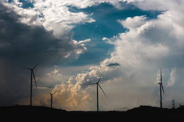 Fototapeta premium Landscape of silhouette wind turbine with a big group white cloud, soft blue sky. Alternative and Clean energy concept.
