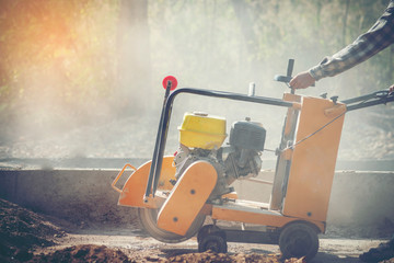 Concrete cutter machine is cutting the cement roadIn the concrete dust cloud to create a track.