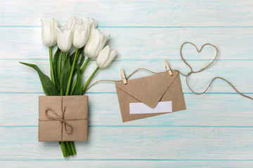 A bouquet of white tulips with a love note and envelope on a heart-shaped rope and blue wooden boards