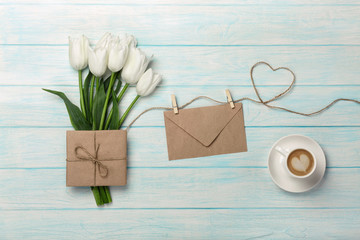 A bouquet of white tulips, cup of coffee with a love note and envelope on a heart-shaped rope and blue wooden boards