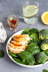 Chicken breast with spinach, broccoli and citrus dressing on a white plate. Grey concrete background. Copy space. Healthy diet lunch or dinner. Keto diet.
