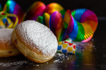 leckere frische Krapfen, Luftschlangen, Rotorspiralen, und Tröten vor schwarzem Hintergrund