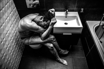Naked man sitting in the old city toilet. Person feels terrible emotional pain and helplessness. The addict feels bad. Black and white picture. - obrazy, fototapety, plakaty