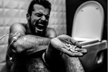 Balck and white picture of young man screaming and yelling on floor in rest room. He suffer. Guy show pills in hand. Drugs addiction. Hand is wrapped with plait. Another dose.