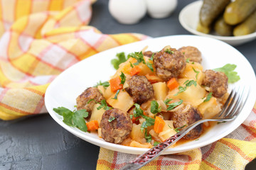Stewed potatoes with meatballs on a white plate