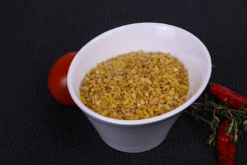 Raw bulgur in the bowl with tomatoes and garlic
