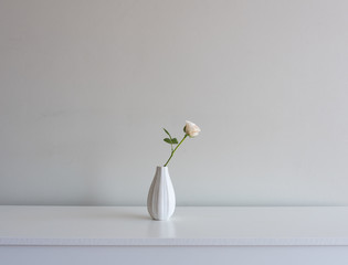 Close up of single pale pink rose in small vase in the centre of white sideboard against neutral...