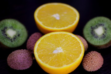 still life of citrus, juicy kiwi and orange in the cut and Litchi chinensis on a dark background