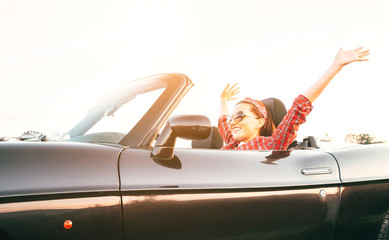 Young laughing female cheerful rising hands up in by cabriolet car in sunny day time