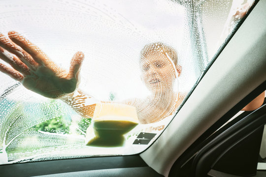 Little Boy washing his family windshield car window with soap foamy sponge. Inside car camera view.