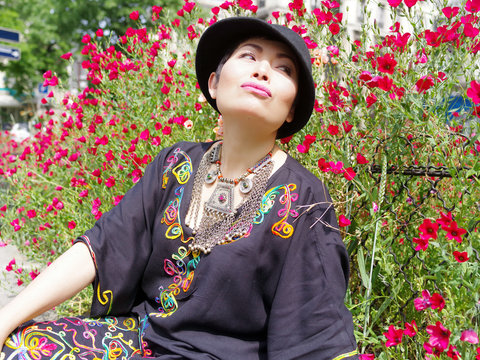 Femme assise et faisant la moue devant un massif de fleurs rouge