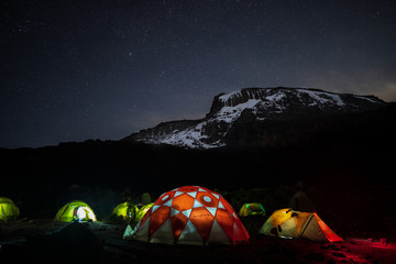 Beleuchtete Zelte in der Nacht vor dem Kilimandscharo