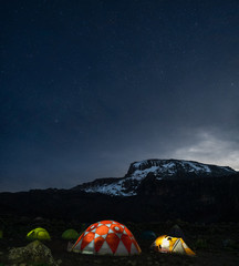 Lighted tents in the night in front of Mount Kilimanjaro