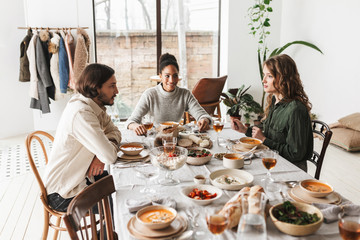 Group of young international friends sitting at the table dreamily talking to each other. Handsome man and beautiful women having lunch spending time together in cozy cafe