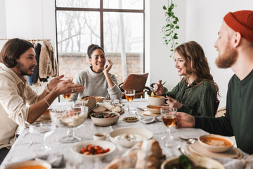 Group of attractive international friends sitting at the table full of food happily talking to each other. Young colleagues joyfully spending time together on lunch in cafe