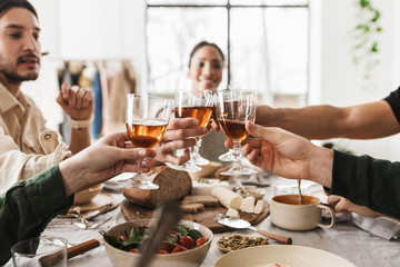 Close up hands of international friends holding glasses of wine. Young colleagues happily celebrating together spending time on lunch in cafe