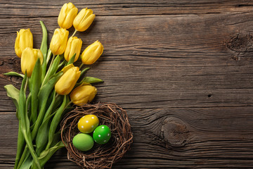 Yellow tulips in a paper bag, a nest with Easter eggs on a wooden background. Top view with copy space.