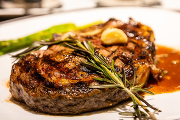 A sprig of rosemary on a fresh roasted bone-in ribeye steak with garlic, gravy and asparagus