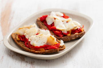 black healthy bread with cod fish and red pepper on dish
