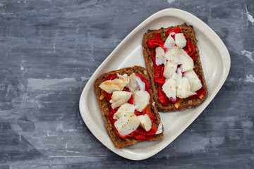 black healthy bread with cod fish and red pepper on dish