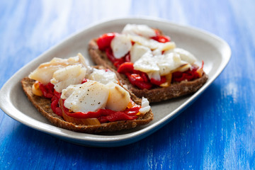 black healthy bread with cod fish and red pepper on dish