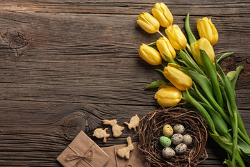 Easter background with colorful eggs and yellow tulips on wooden table. Top view with copy space