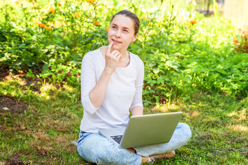 Freelance business concept. Young woman sitting on green grass lawn in city park working on laptop pc computer. Lifestyle authentic candid student girl studying outdoors. Mobile Office