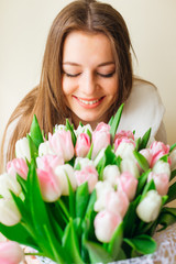Close up of young woman closes her eyes and smiles at large pink tulips flowers bouquet. Sunny spring morning.