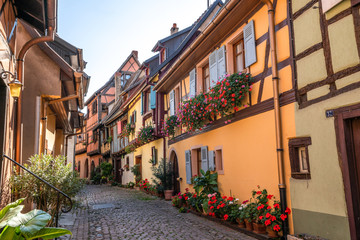 Fototapeta na wymiar Cobblestone street in picturesque Alsace village with half timbered houses and beautiful flowers. 