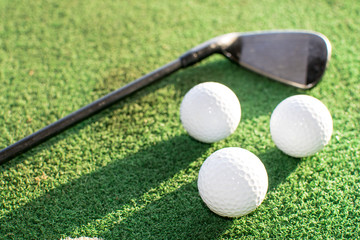 Three golf balls and a golf club on a green artificial grass
