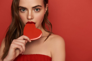 Cropped photo of young woman touching her lips with decorative heart indoors