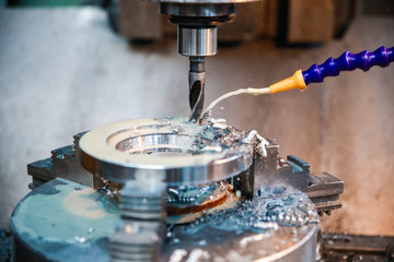 Drilling machine makes a hole in the metal product. Coolant is pouring on the drill.