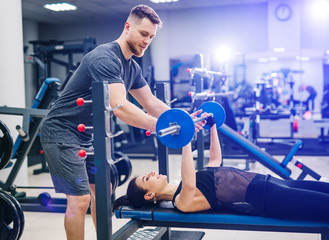 Fitness girl having weight training with assistance of coach in gym. Personal fitness instructor....